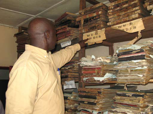 A health worker looking through archived paper reports where some of the reports are visibly torn or in bad condition.